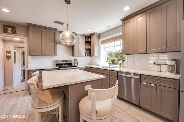 kitchen featuring a kitchen island, a breakfast bar, stainless steel appliances, light countertops, and a sink