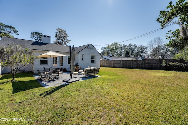 back of house with a patio, a lawn, a chimney, and fence