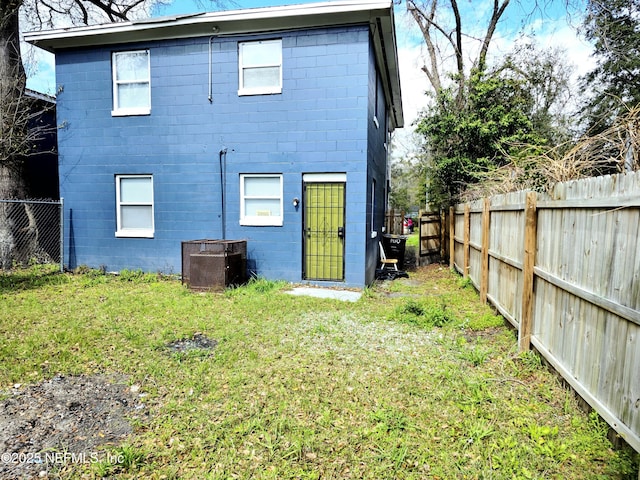 back of property with a lawn, concrete block siding, and central air condition unit