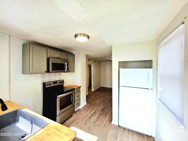 kitchen with a textured ceiling, stainless steel appliances, a sink, light wood-style floors, and gray cabinets