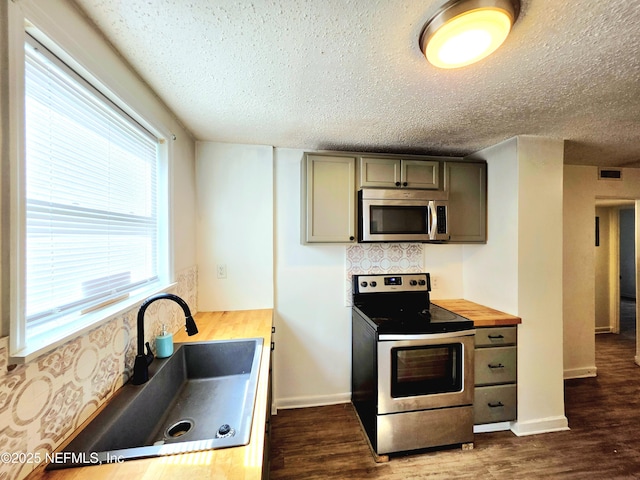 kitchen with appliances with stainless steel finishes, butcher block countertops, a sink, and dark wood-style floors