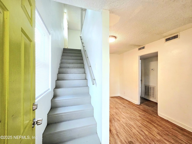 staircase with a textured ceiling, wood finished floors, visible vents, and baseboards