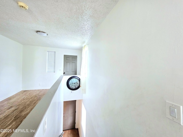 hall featuring a textured ceiling, baseboards, and wood finished floors