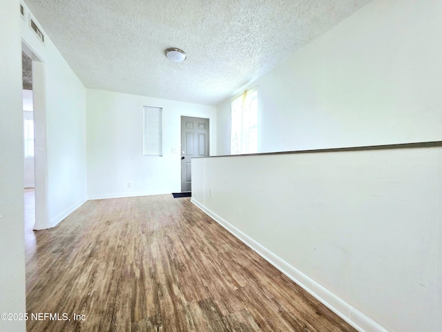 spare room with visible vents, a textured ceiling, baseboards, and wood finished floors