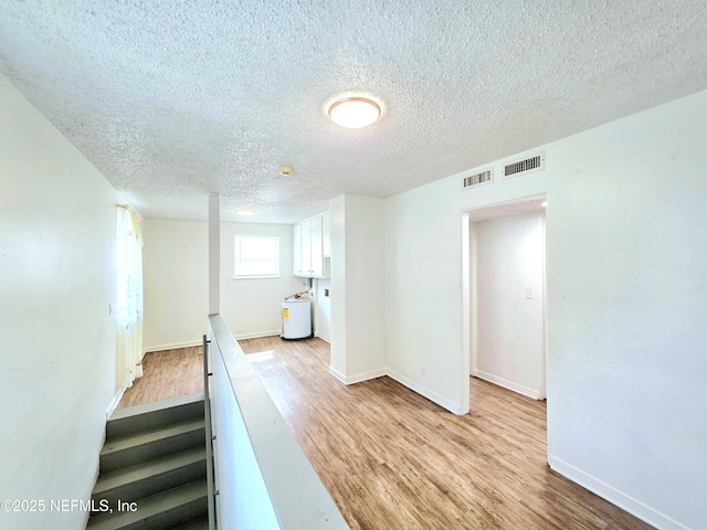 hall featuring light wood-type flooring, visible vents, and baseboards