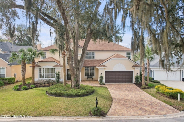 mediterranean / spanish-style home with a garage, a chimney, decorative driveway, a front lawn, and stucco siding