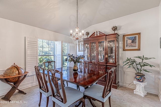 dining area featuring a chandelier, vaulted ceiling, wainscoting, light tile patterned flooring, and a decorative wall