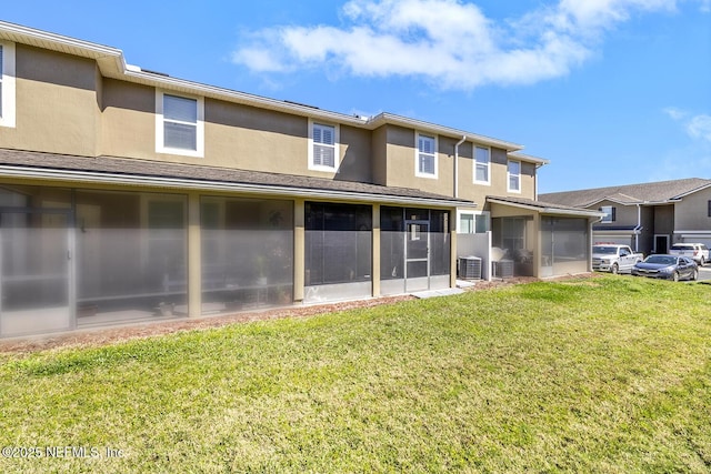 back of property featuring a sunroom, a yard, central AC, and stucco siding