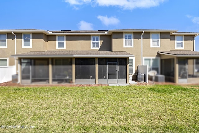 back of property with a sunroom, a lawn, central air condition unit, and stucco siding