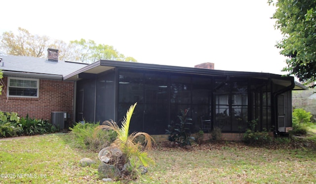 back of house featuring brick siding, a chimney, and a sunroom