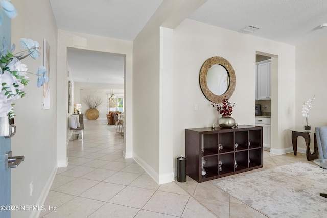 corridor with a textured ceiling, baseboards, and light tile patterned floors