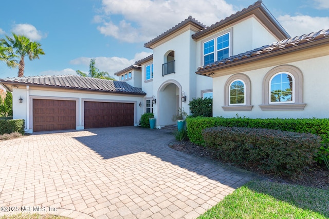 mediterranean / spanish home with a garage, a tiled roof, decorative driveway, and stucco siding