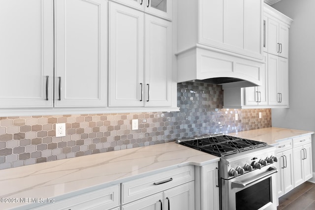 kitchen with high end stove, tasteful backsplash, white cabinetry, and light stone counters