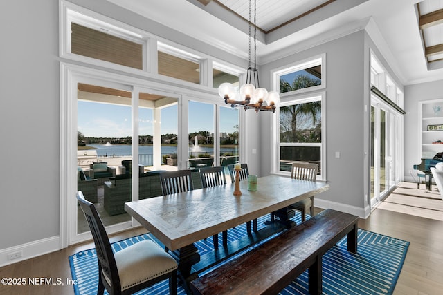 dining area with a water view, a chandelier, wood finished floors, and ornamental molding