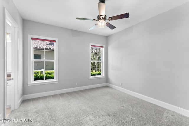 carpeted spare room featuring baseboards and a ceiling fan