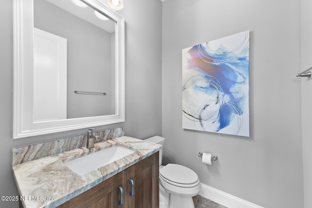 half bathroom with vanity, toilet, and baseboards