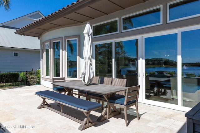 view of patio with outdoor dining space, a water view, and fence