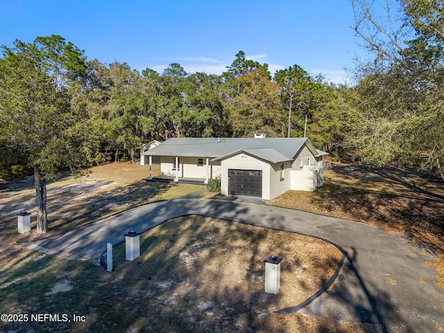 view of front of house with an attached garage, a view of trees, concrete driveway, and stucco siding