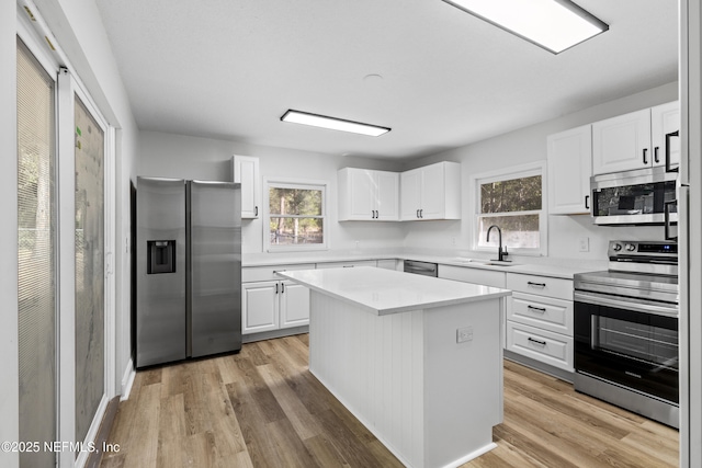 kitchen featuring light wood-style flooring, stainless steel appliances, a sink, light countertops, and a center island