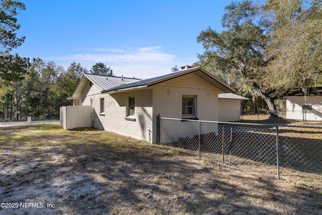 view of side of property with fence, metal roof, and brick siding