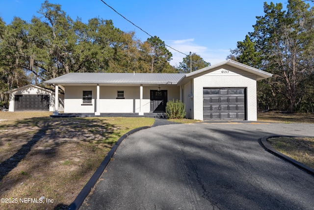 ranch-style house featuring aphalt driveway, metal roof, an attached garage, a porch, and brick siding