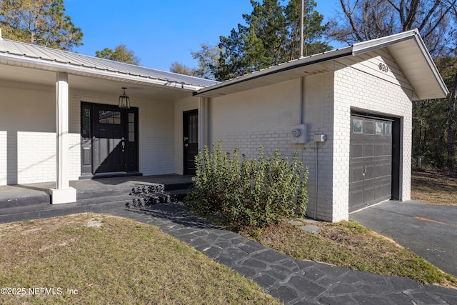 doorway to property featuring metal roof, brick siding, a porch, and driveway