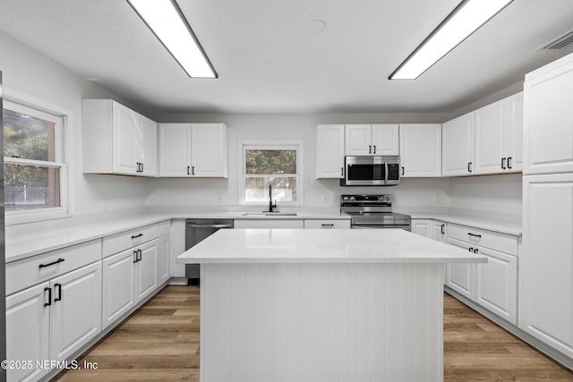 kitchen with appliances with stainless steel finishes, visible vents, a kitchen island, and light wood finished floors