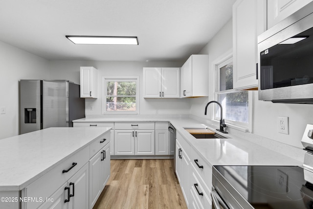 kitchen featuring a sink, white cabinetry, light wood-style floors, appliances with stainless steel finishes, and a center island