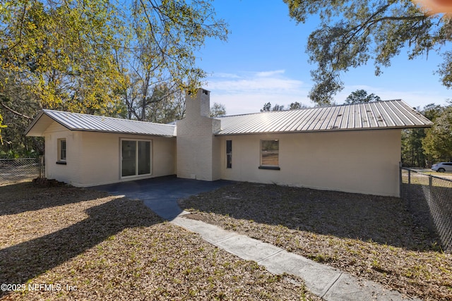 rear view of property with metal roof, a chimney, a patio, and a fenced backyard