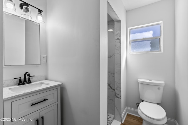 bathroom with baseboards, toilet, wood finished floors, a tile shower, and vanity