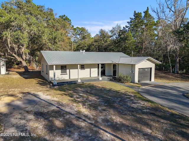 ranch-style home with metal roof, a porch, aphalt driveway, a garage, and stucco siding