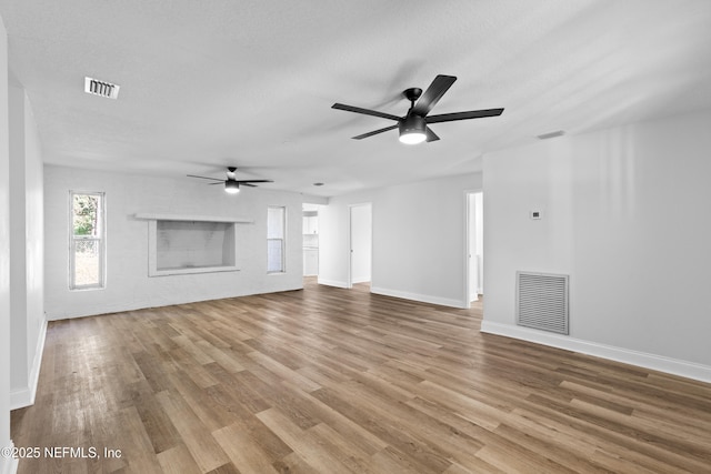 unfurnished living room with visible vents, a fireplace, baseboards, and wood finished floors