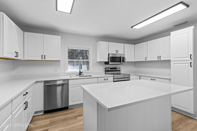 kitchen with stainless steel appliances, light countertops, light wood-style flooring, white cabinetry, and a sink