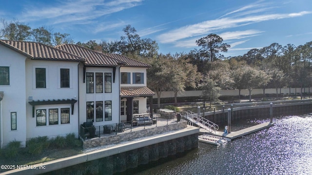 back of property with a water view, stucco siding, fence, and a tiled roof