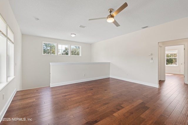 empty room with a ceiling fan, baseboards, visible vents, and dark wood-type flooring