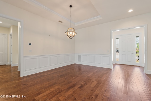 interior space with dark wood-type flooring, a raised ceiling, a wainscoted wall, and crown molding