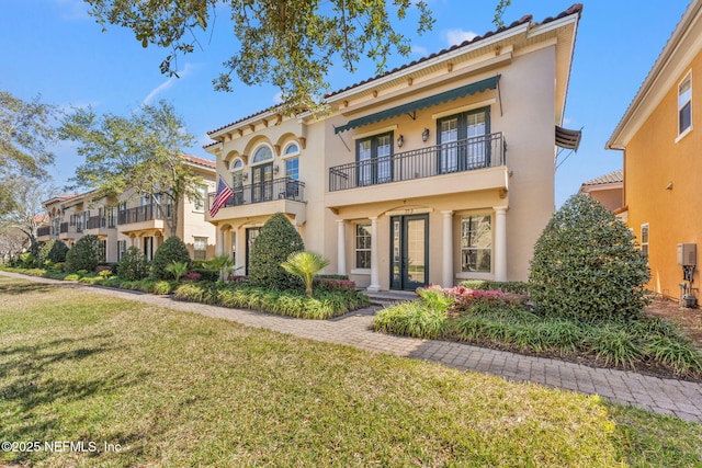 mediterranean / spanish home featuring a tile roof, a balcony, a front lawn, and stucco siding