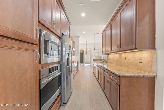 kitchen with light stone counters, a sink, appliances with stainless steel finishes, light wood finished floors, and tasteful backsplash