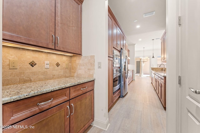 kitchen featuring tasteful backsplash, light wood-style flooring, stainless steel microwave, light stone counters, and a sink