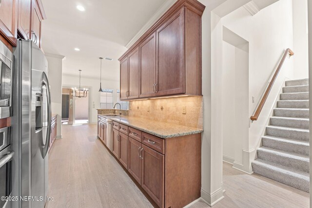 kitchen with a chandelier, light stone countertops, appliances with stainless steel finishes, light wood-type flooring, and decorative backsplash