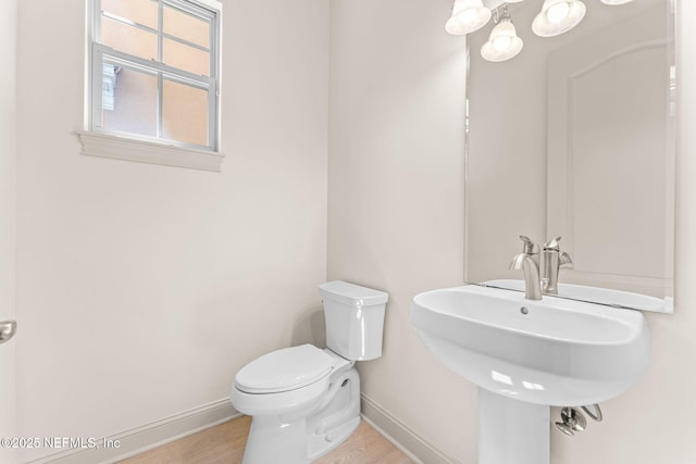 half bath featuring a sink, wood finished floors, toilet, and baseboards