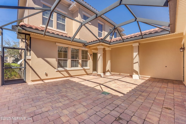 rear view of house featuring glass enclosure, a patio area, a tile roof, and stucco siding