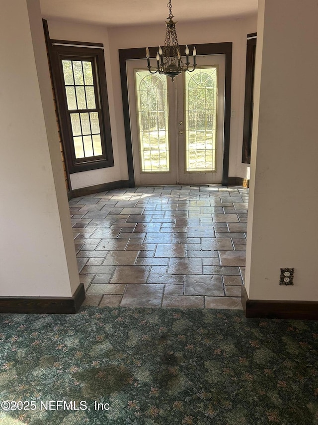 doorway to outside with a chandelier, french doors, stone tile flooring, and baseboards