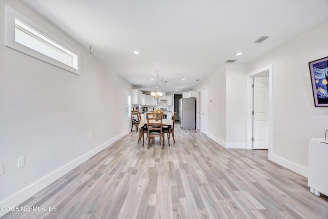 unfurnished dining area featuring baseboards, light wood-style floors, visible vents, and a chandelier