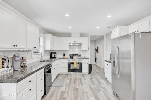 kitchen featuring a sink, stainless steel appliances, white cabinets, under cabinet range hood, and backsplash