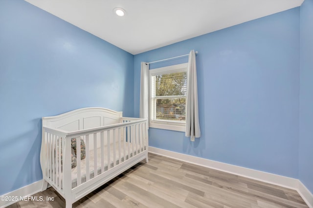 bedroom with recessed lighting, a crib, baseboards, and wood finished floors