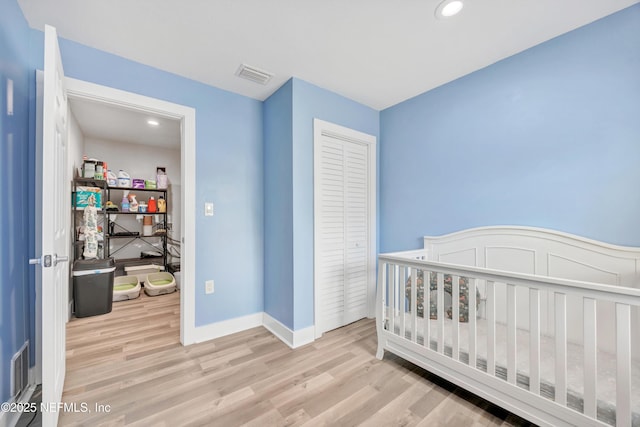 bedroom with wood finished floors, visible vents, a closet, and baseboards