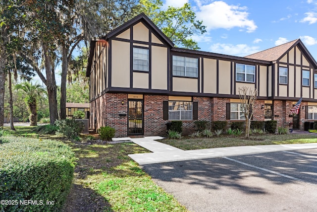 english style home featuring uncovered parking, brick siding, and stucco siding