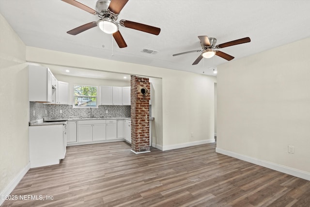 unfurnished living room with a sink, light wood-style flooring, visible vents, and ceiling fan