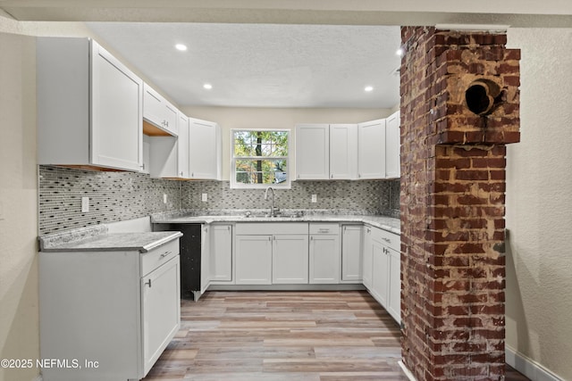 kitchen with light wood-style flooring, a sink, tasteful backsplash, a textured ceiling, and white cabinets